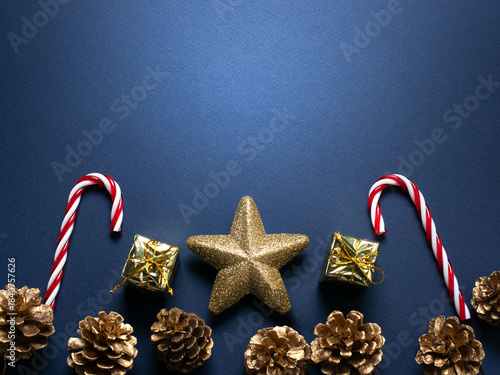 Christmas minimalistic dark blue background with decorative candy canes, glittering stars, golden gift boxes and pine cones for tree decoraton. New Year winter holiday decor and copy space, top view.