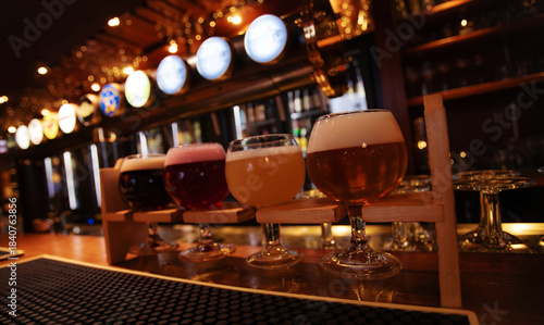 Photos A selection of craft beers in tasting glasses placed on a wooden rack at a bar counter