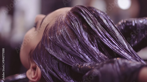 a person with purple glossy hair, likely in a salon or styling environment, given the presence of styling tools and products. the hair appears to be freshly styled with a shiny, glossy texture