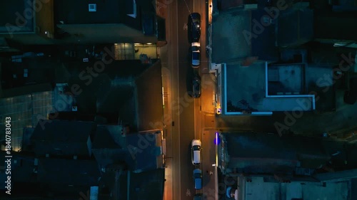 Aerial view of a street at night, with cars and buildings illuminated by streetlights.