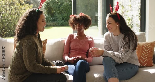 Diverse female friends breaking silence on sofa sharing animated anecdote with headbands and mug