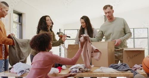 Friends in volunteer room passing tape sorting and folding sweaters into Donation boxes on table