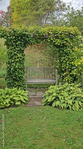 Park bench under outdoor archway with plants blowing in wind vertical video
