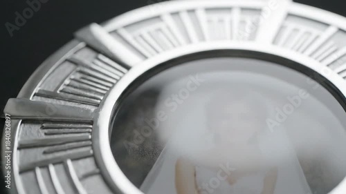A close-up macro shot of a person's blurry portrait within a silver, round, decorative frame