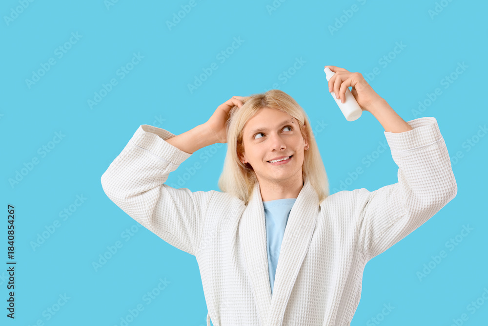 Fototapeta premium Young blonde man with hair spray on blue background