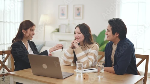 Estate agent hands house keys to the client. Asian woman realtor gives keys to the couple buyer while sitting at a table with a house model. Real estate.