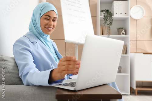 Young Muslim businesswoman learning Arabic language online on sofa in office