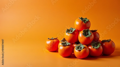 A stack of persimmons on a plain, bright orange background with plenty of white space on the left. Banner, advertising.