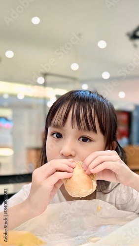 Portrait of adorable child looking at camera while eating burger, unhealthy meal but tasty.