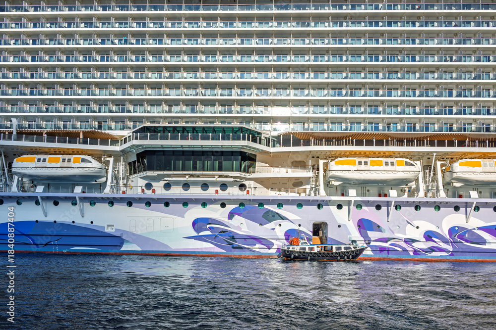 Obraz premium A tender boat pulls up next to a large cruise ship as it prepares to take passengers from the sea to the port.