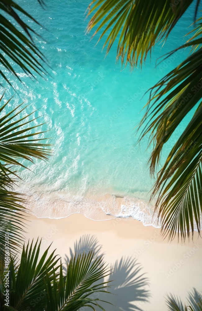 Fototapeta premium Palm leaves frame view of calm ocean waves washing ashore on a white sand beach. Turquoise water shimmers under sunny sky. Tropical paradise scene.