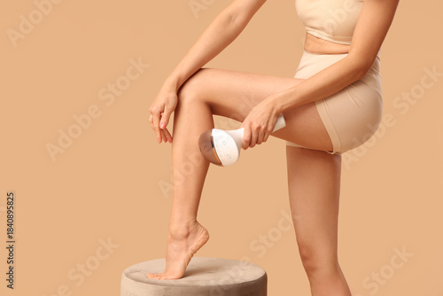 Photos Young woman using photoepilator on legs against beige background
