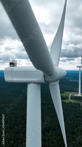 Close-up of a wind turbine with forest and cloudy sky in the background