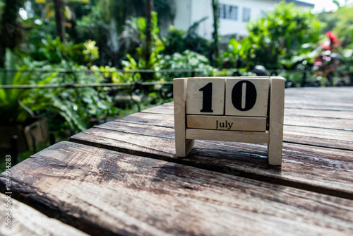 Wooden cube calendar for 10th July place on a table in a sunny garden background