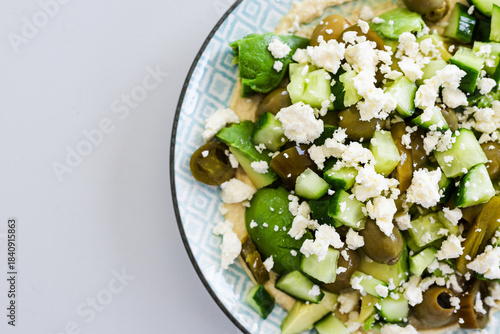 healthy nourish bowl with avocado, jalapeno, feta, green olives and cucumber on hummus