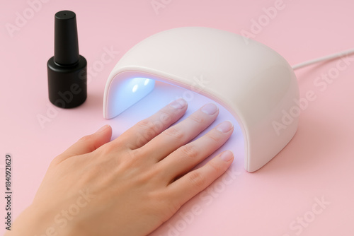 Woman curing gel nail polish under led lamp on pink background during home manicure session
