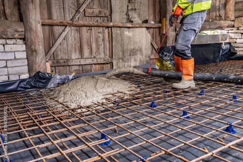 A groundworker skillfully pours concrete onto a metal grid at a construction site. This image highlights the crucial step of laying a solid foundation for building projects.