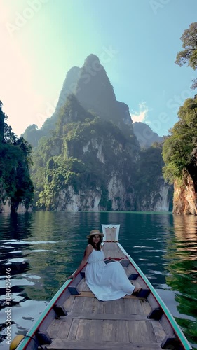 Discover the breathtaking landscapes of Khao Sok, Thailand, as an Asian woman relaxes on a boat, surrounded by stunning mountains and calm waters under a bright sky.
