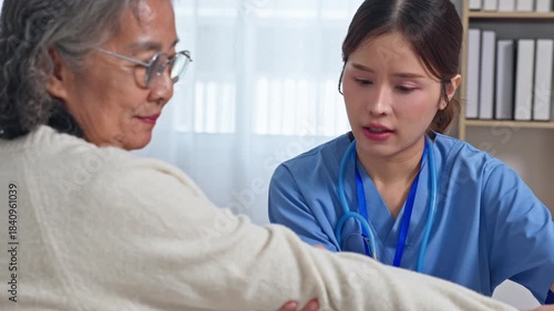 Asian compassionate caregiver assisting elderly woman with arm exercise and physical therapy at home care rehabilitation while nurse conducts gentle examination with stethoscope