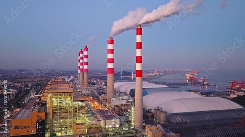 Aerial shot of thermal power plant with smoking chimneys and illuminated industrial buildings at sunset