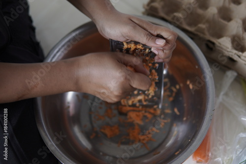 Hands grating fresh carrots into a metal bowl for cooking