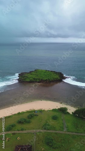 Aerial footage of a pristine and stunningly beautiful beach area. Drone footage captures the beach, featuring expansive green grass, pristine white sand, and a small island just off the mainland.