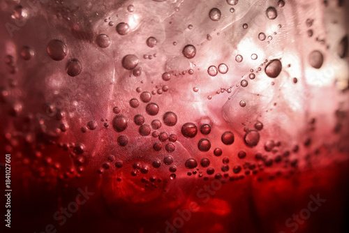 Macro closeup of refreshing red drink with ice and bubbles. carbonated soda beverage and fizzy liquid texture create an intense, moody background for any project