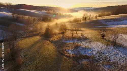 Golden sunrise over misty winter valley rolling hills bare trees frosted fields serene landscape aerial drone view