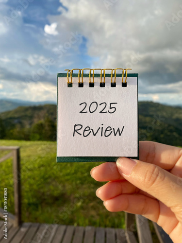 Hand holding note pad with the number “2025 Review” with blurry nature background. Concept for performance review, growth analysis, end-year reflection and planning, business summary and annual report