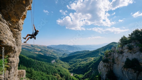 Rock climber rappels down steep cliff face overlooking vast forested mountain valley vista