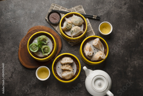 Photos An overhead shot of a delicious assortment of steamed dim sum dumplings in bamboo baskets, served with hot tea on a dark table
