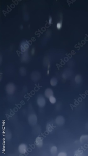Abstract blue bokeh background with soft glowing light particles falling in dark space