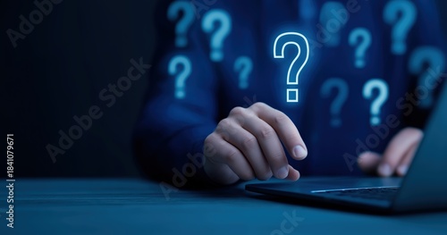 Question mark graphic over person using laptop computer for online support and problem solving in dark blue tones conceptual image