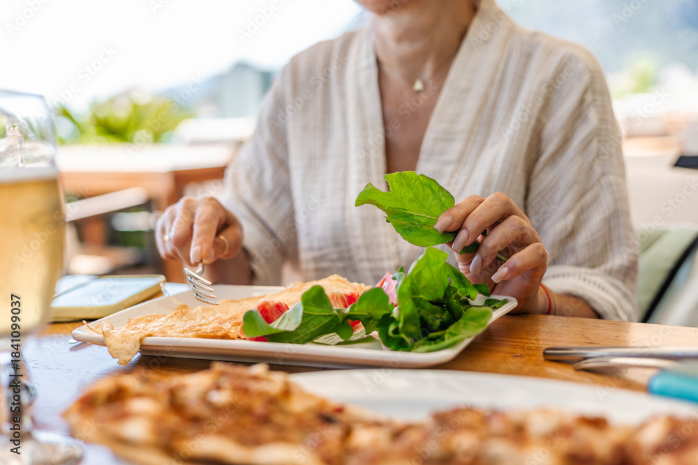Naklejka premium Woman is seated at a table with plate of salad and glass of drink