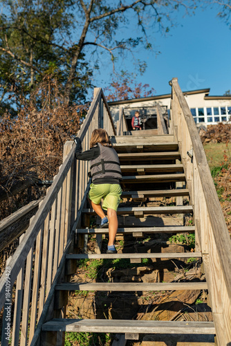 child in life jacket walking up sunlit wooden stairs