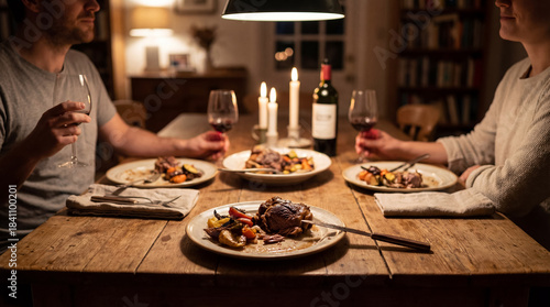 Two individuals are enjoying a delightful candle lit dinner with glasses of wine at a wooden table. Each person has a plate of roasted meat and vegetables.