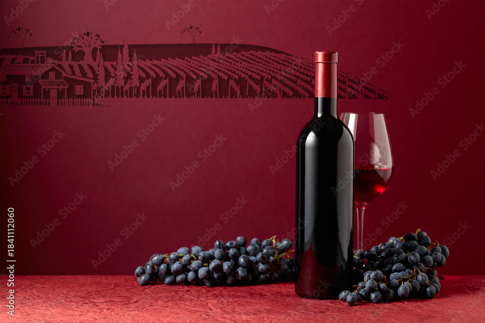 Fototapeta premium Bottle and glass of red wine with blue grapes on a red background.