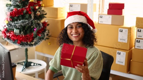 Small business warehouse, Christmas season with female staff offering festive gift, presenting holiday package with cheerful expression and supporting ecommerce order preparation in seasonal workspace