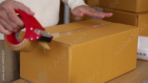 Warehouse shipping workflow showing young worker attaching label to parcel, preparing delivery orders, managing ecommerce packing process, supporting logistics operation in small business storehouse