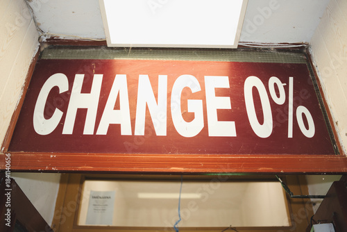 Red sign with white text change 0 percent hangs above a commercial counter in an old, run down office, representing concepts of stagnation, resistance, and financial immobility