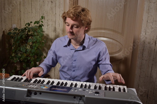 A young white man plays an electronic synthesizer indoors, immersed in his creative hobby. Focused on shaping tones and melodies, he explores musical expression and artistry in a calm home setting.
