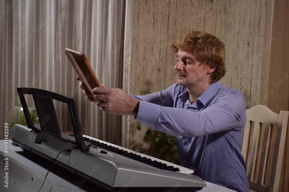 Fototapeta premium A young white man plays an electronic synthesizer indoors, immersed in his creative hobby. Focused on shaping tones and melodies, he explores musical expression and artistry in a calm home setting. 
