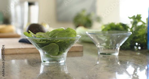 Camera is pushing in and adjusting focus, bringing glass bowl of spinach into focus on countertop