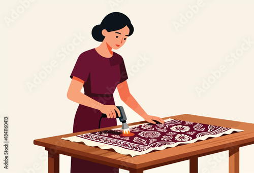 A woman is using a tool to work on a patterned textile. She works at a wooden table