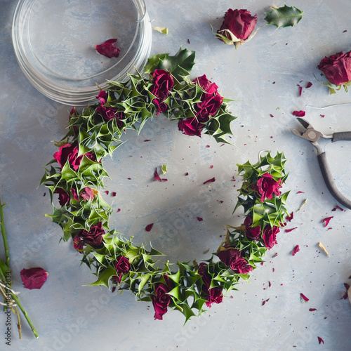 A winter wreath made of dried roses and holly leaves in the process of being made