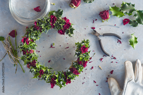 A winter wreath made of dried roses and holly leaves in the process of being made
