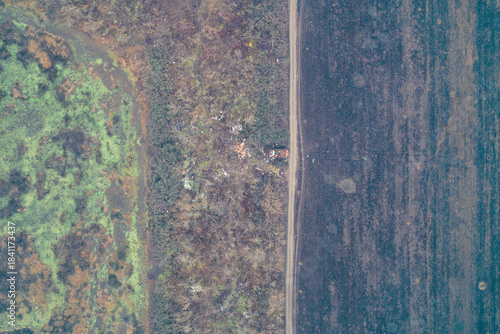 Bild auf Leinwand Top-down aerial view of straight road separating burnt scrubland and tilled field with military debris