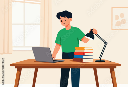 A person in a green shirt works on a laptop, with books and a desk lamp on the table. A window and art are present