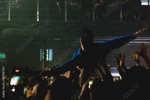 Young person lifted by audience during an energetic live music event with cheering crowd and dynamic lighting.