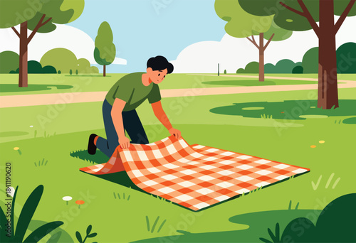 A person in a park kneels to lay out a picnic blanket on a green lawn, trees surrounding